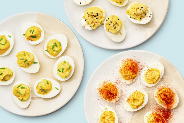 Three white plates with instant pot deviled eggs with various toppings are on a blue background.