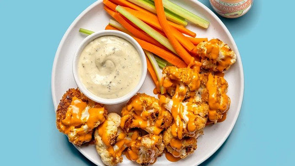 A plate of Buffalo cauliflower wings with a ramekin of Primal Kitchen Ranch Dressing. 