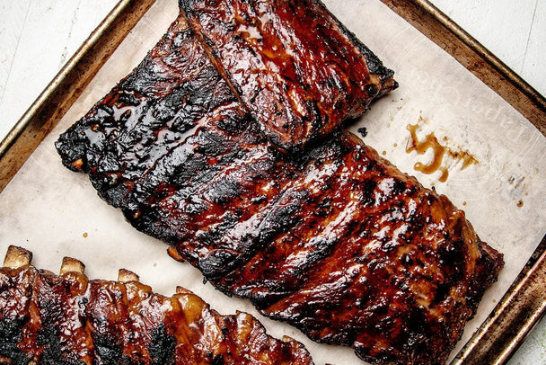 Spare ribs coated in Primal Kitchen Thick & Sticky Honey Teriyaki Sauce on a baking sheet lined with parchment. 