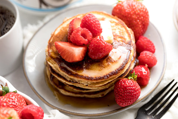 A stack of pancakes made with Primal Fuel Vanilla Coconut Whey Protein, topped with berries, butter, and syrup.  