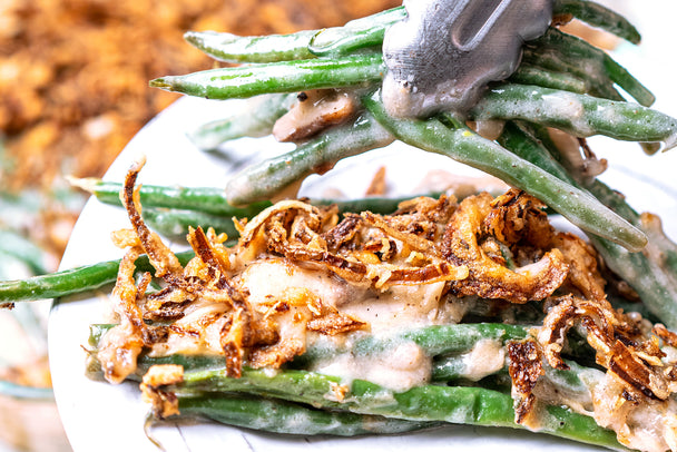 Tongs putting a serving of green bean casserole on a white plate.