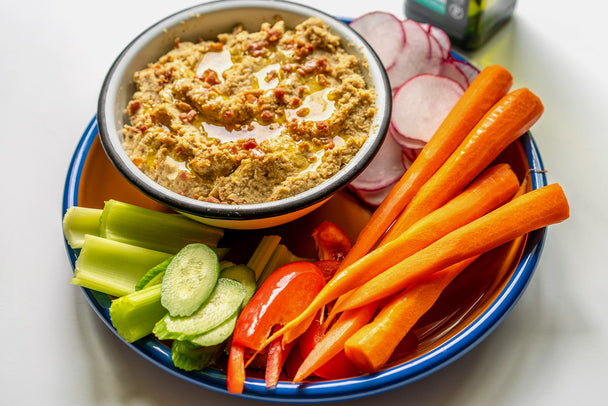 A bowl of cauliflower and macadamia nut hummus on a plate with raw vegetables. 