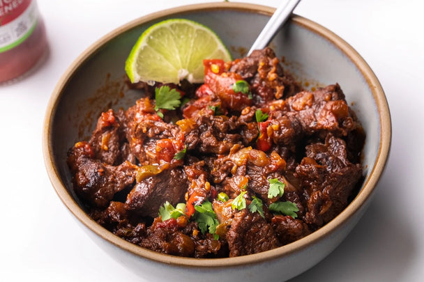 Keto no bean chili is in a white bowl with a silver spoon and a spicy ketchup bottle next to it.