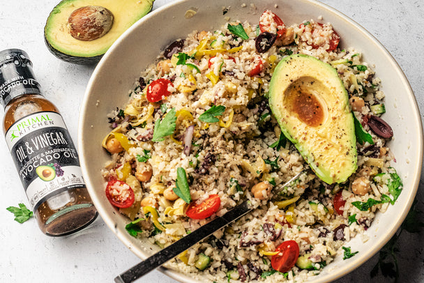 Pulled out version of Keto Vegan Mediterranean bowl in a large white bowl with a fork in it. Primal Kitchen Avocado Oil & Vinegar Vinaigrette and half an avocado next to the bowl.