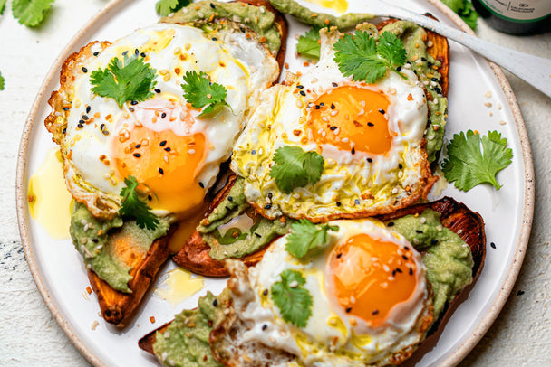 Sweet potato toasts with smashed avocado and eggs on a white plate next to Primal Kitchen Extra Virgin Avocado Oil