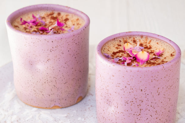 Two mocha lattes topped with cacao powder and organic rose petals in lavender mugs.