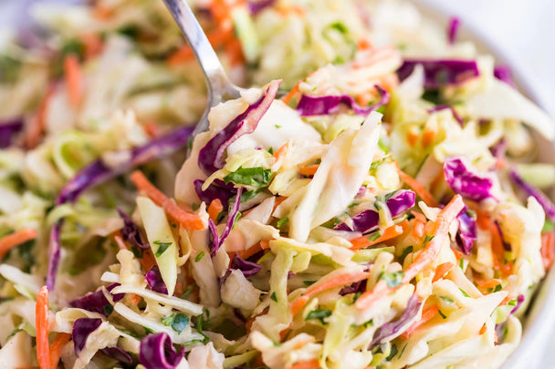 Closeup of spooning into a dish of Easy Coleslaw made with creamy Primal Kitchen Mayo. 