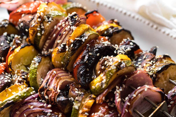 A white tray of vegetable skewers next to a bottle of Primal Kitchen No-Soy Teriyaki Sauce.  