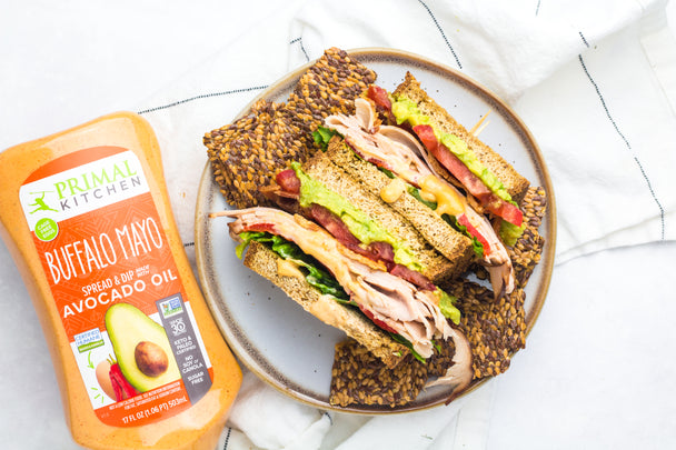 A Turkey avocado sandwich cut in half on a plate next to a Squeeze Buffalo Mayo bottle