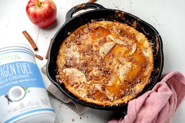 Apple cinnamon Primal pancake in a cast-iron skillet next to Primal Kitchen Collagen Fuel, an apple and cinnamon stick