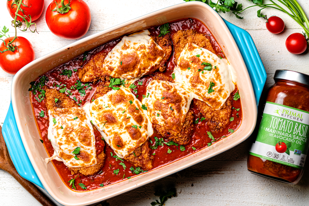 Keto Chicken Parmesan in a blue dish is surrounded by tomatoes and tomato basil pasta sauce.