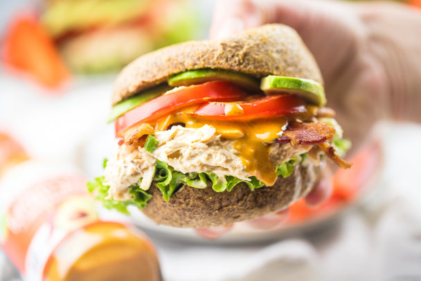 Buffalo Chicken Sandwich with Bacon cut in half and stacked on a plate which a hand reaches for the top half.