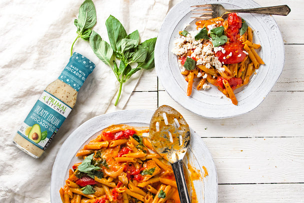 Two plates of Italian Pasta next to a bottle of Primal Kitchen Dreamy Italian Dressing. 