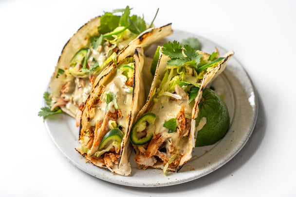 Three chicken tacos drizzled with with Primal Kitchen Avocado Lime Ranch, on a white plate. 