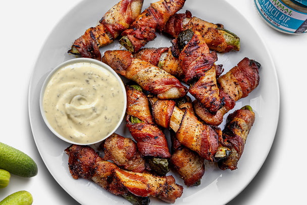 Up close shot of a plate of bacon wrapped pickles with a side of Primal Kitchen No Dairy Ranch Dip