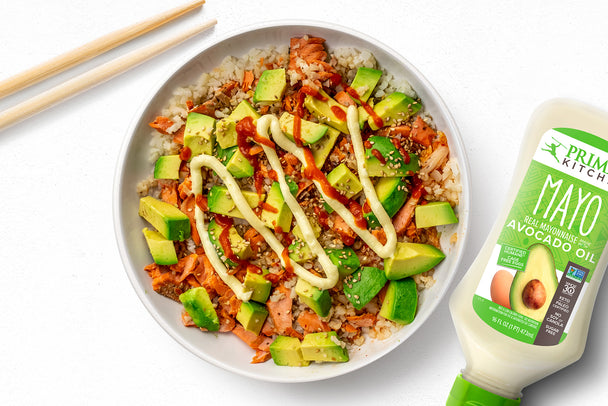 Salmon bowl topped with Primal Kitchen Mayo, sitting on a white table next to a squeeze bottle of Primal Kitchen Mayo