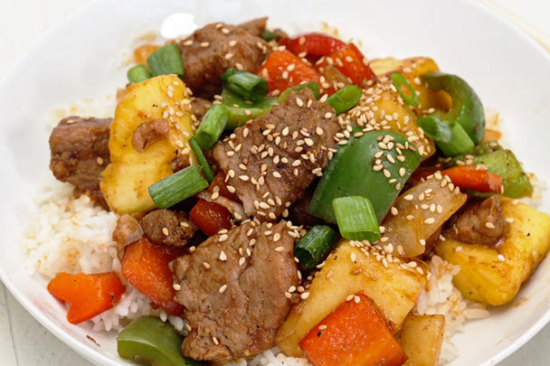 Sweet and Sour pork is served on a bed of rice on a white plate.