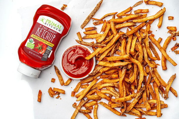 Crispy air fried french fries next to a ramekin of ketchup and a squeeze bottle of Primal Kitchen A Tad Sweet Ketchup.