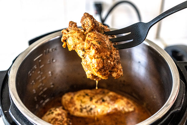 A fork with a bite of chicken over an Instant Pot filled with Ranch Chicken.