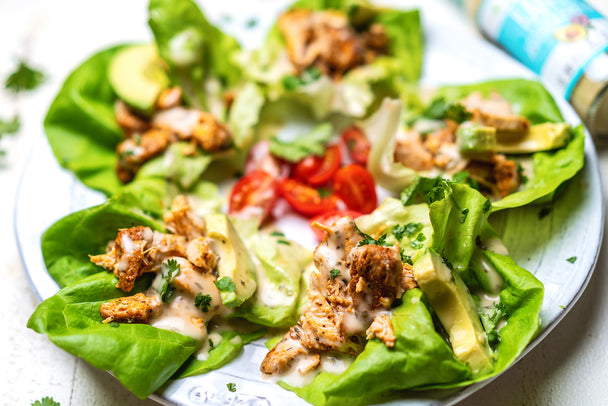 Instant Pot shredded chicken with ranch piled on butter lettuce cups on a big plate. The chicken lettuce cups have avocado slices and sliced cherry tomatoes.