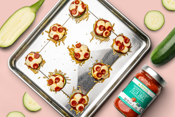 Air Fryer Pizza bites are assembled on a silver baking tray with pizza sauce and zucchini slices nearby.