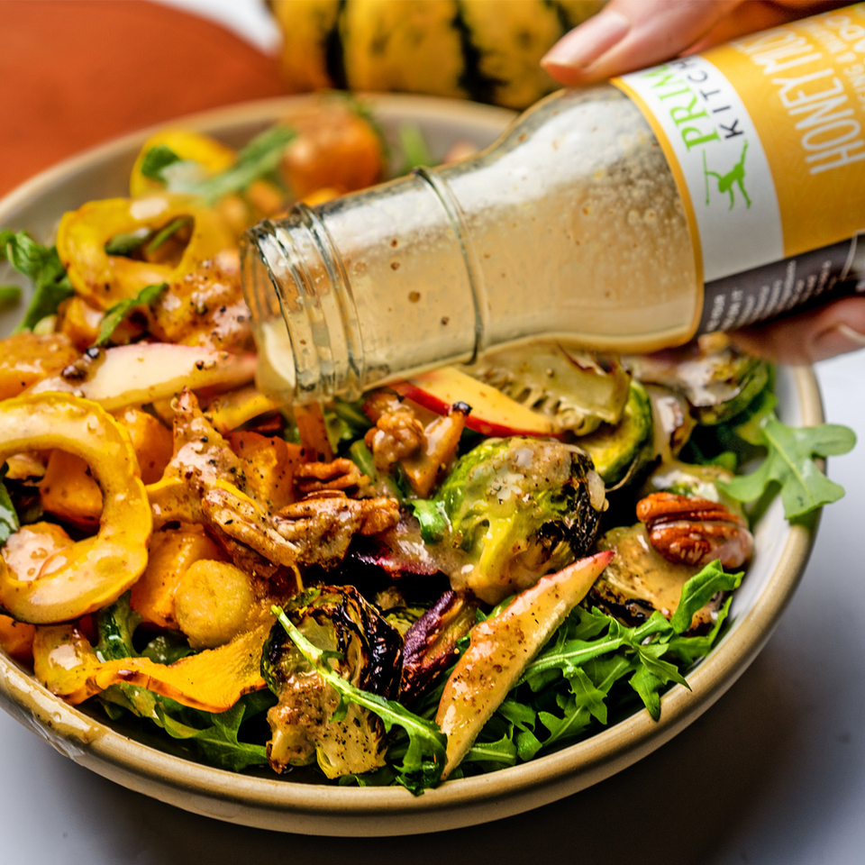 A harvest bowl being topped with Primal Kitchen Honey Mustard Vinaigrette & Marinade made with Avocado Oil.