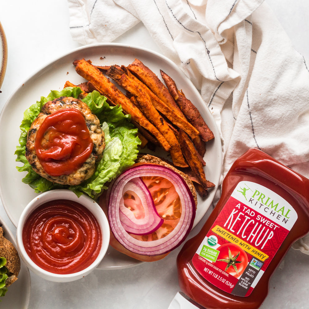 An Air Fryer Turkey burger topped with Ketchup, next to a bottle of Primal Kitchen Tad Sweet Ketchup.