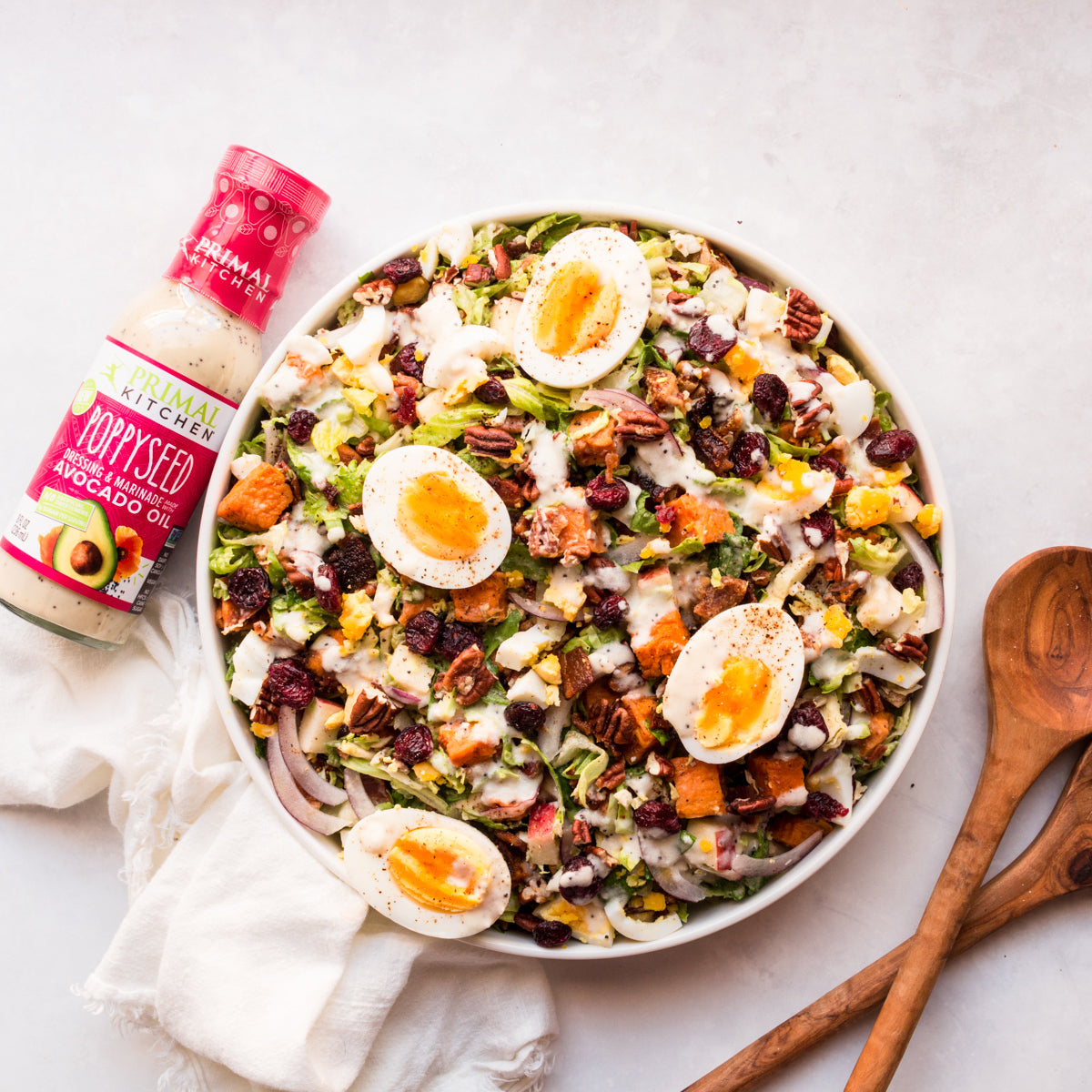 A bottle of Primal Kitchen Poppyseed Dressing next to a bowl of autumn salad.