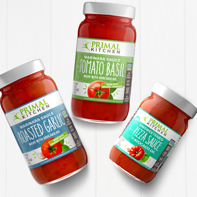 Jars of Primal Kitchen Roasted Garlic Marinara Sauce, Primal Kitchen Tomato Basil Marinara Sauce, and Primal Kitchen Unsweetened Red Pizza Sauce on  a light grey background.