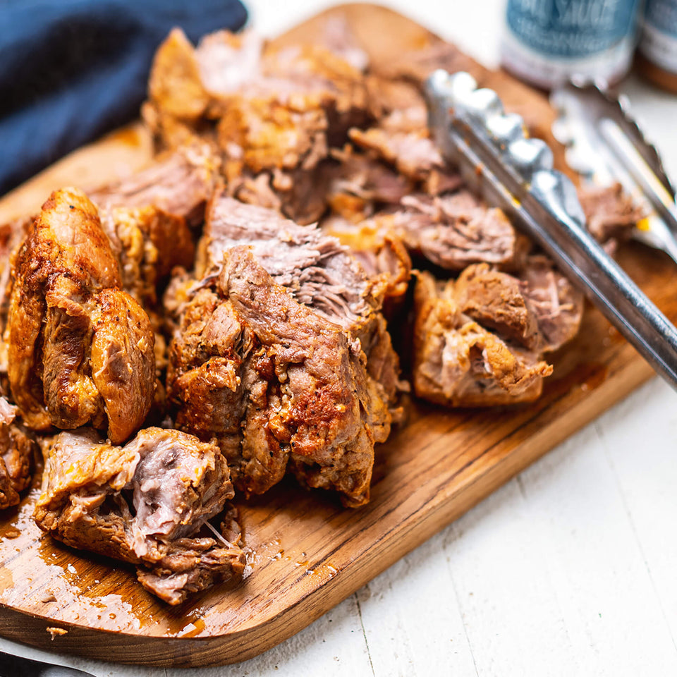 Instant Pot Pulled Pork on a wood cutting board with a metal spatula and Primal Kitchen Organic Unsweetened Golden BBQ Sauce in the background