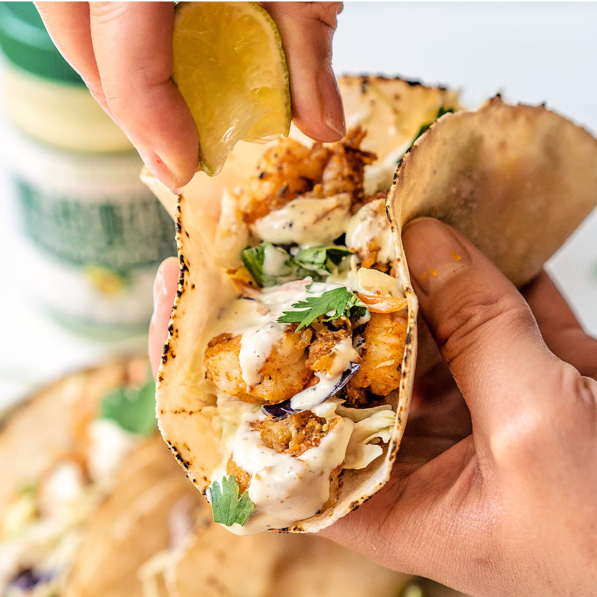 Person squeezing lime on to a fish taco with Primal Kitchen Pesto Mayo blurred in the background.