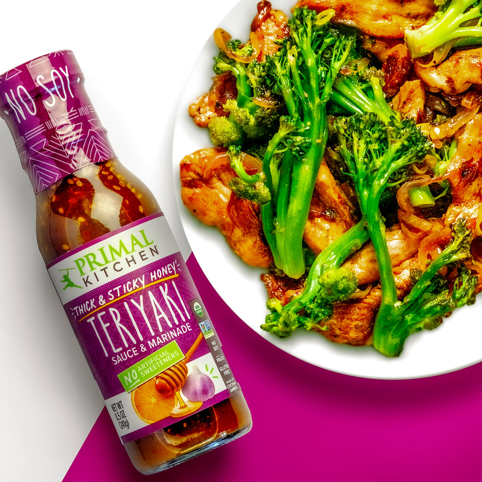 A white plate with stir fry chicken and broccolini alongside Primal Kitchen Thick & Sticky Honey Teriyaki Sauce & Marinade on a purple and white background